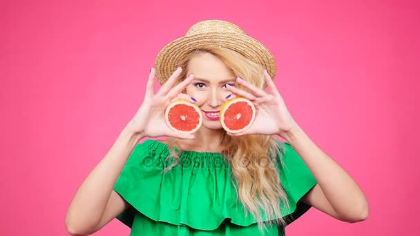 Joven mujer feliz sostiene rodajas de pomelos en sus ojos sobre fondo rosa — Vídeo de stock