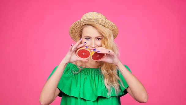Jovem mulher feliz está segurando fatias de toranja em seus olhos no fundo rosa — Vídeo de Stock