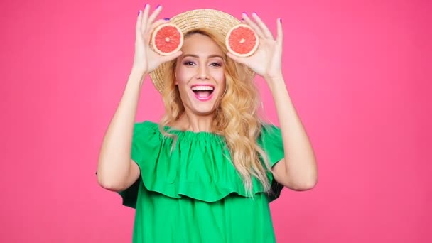 Joven mujer feliz sostiene rodajas de pomelos en sus ojos sobre fondo rosa — Vídeos de Stock