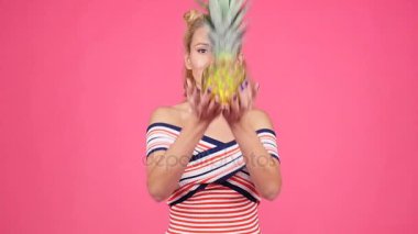 Bir ananas pembe bir arka plan üzerinde tutan genç kadın