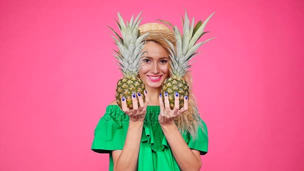Jovem mulher de chapéu segurando um abacaxi em um fundo rosa — Vídeo de Stock
