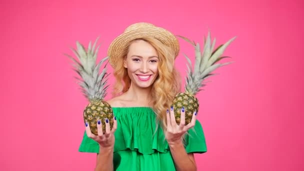 Mujer joven con sombrero sosteniendo una piña sobre un fondo rosa — Vídeo de stock