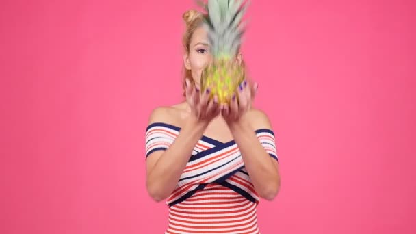 Νεαρή γυναίκα κρατώντας ένα ανανά σε ροζ φόντο — Αρχείο Βίντεο
