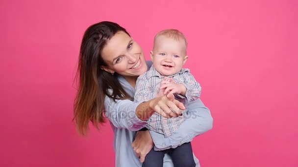 Joven mujer feliz abrazando a su pequeño hijo sobre un fondo rosa — Vídeos de Stock