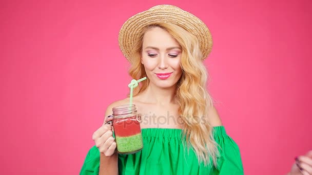 Jovem está segurando um copo com smoothie em um fundo rosa — Vídeo de Stock