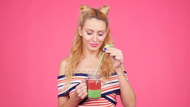 Ung kvinna håller ett glas med smoothie på en rosa bakgrund — Stockvideo