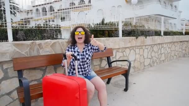 Jeune femme assise sur un banc avec valise — Video