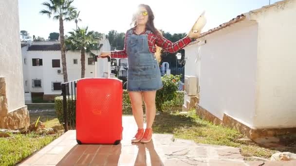 Портрет молодой женщины, позирующей с чемоданом возле курорта — стоковое видео