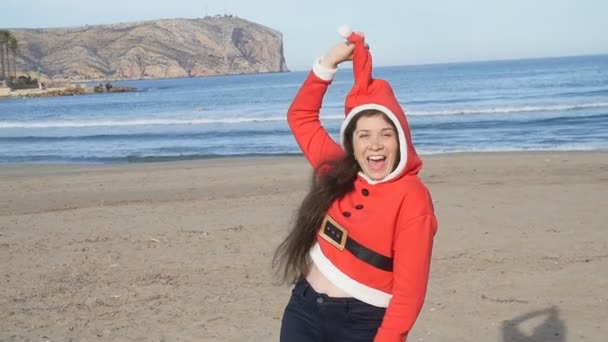 Jovem atraente em santa claus chapéu dançando e se divertindo na praia — Vídeo de Stock