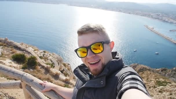 Mladík bere cestování selfie na pěší výlet den. Na pozadí moře a skály — Stock video