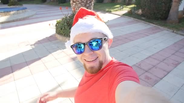 Junger Mann mit Weihnachtsmannmütze im Urlaub. Selbstporträt — Stockvideo