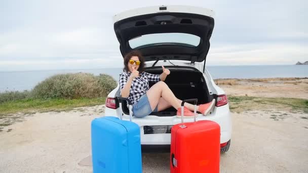 愉快的年轻妇女在夏天旅行假期坐在汽车树干 — 图库视频影像
