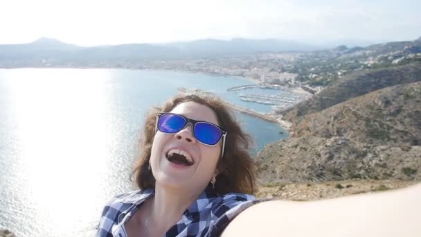 サングラスの幸せな女性旅行者は、海と山の景色と selfie — ストック動画