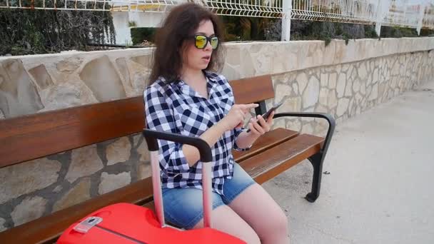 Mujer joven viajero se sienta y mira el teléfono inteligente — Vídeo de stock
