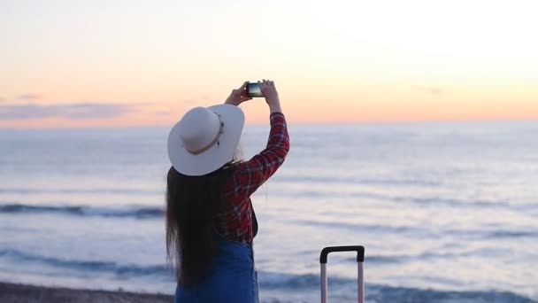 Mladá žena fotografování na pláži při západu slunce nebo sunrise — Stock video