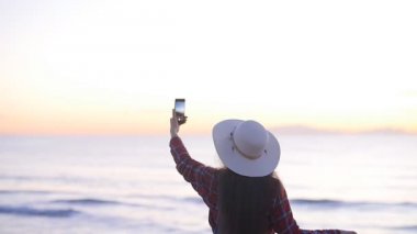 Genç kadın turist tarafından deniz günbatımı veya şafak fotoğrafını çekmek