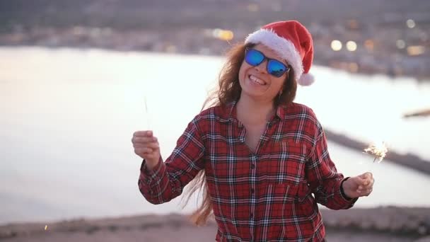 Young woman in christmas or new year coat and hat holding winter holiday sparkler and bengal fire outdoors — Stock Video