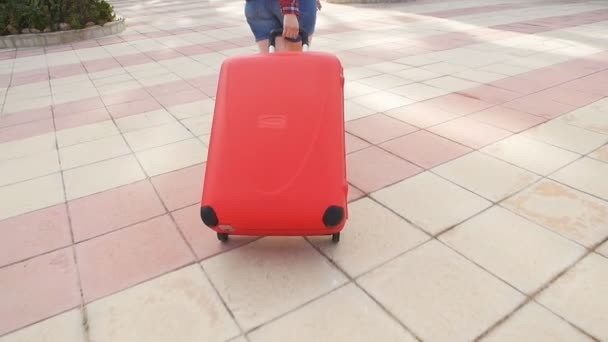 Toung woman with a red suitcase running on a resort — Stock Video