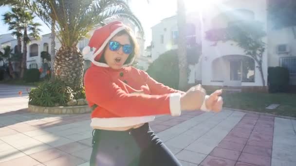 Концепция Рождества и людей - счастливая молодая девушка в зимней шапке возле елки, весело проводящая время на свежем воздухе — стоковое видео