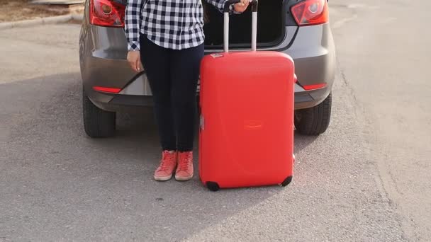 Молода жінка, яка подорожує з валізою, стоїть біля її машини — стокове відео