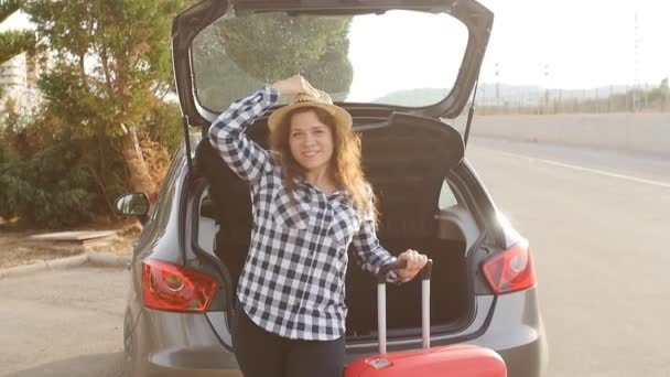 En ung kvinna resenär med en resväska står nära sin bil — Stockvideo