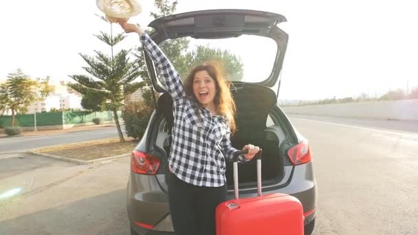 Молодая женщина-путешественница с чемоданом стоит рядом со своей машиной — стоковое видео