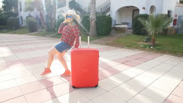 Jovencita feliz con maleta roja llegando al resort o apartamento — Vídeos de Stock