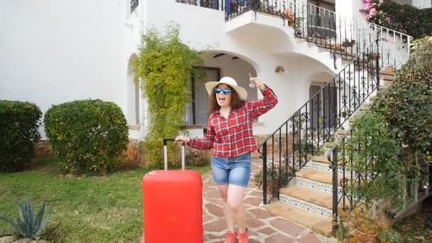 Jovencita feliz con maleta roja llegando al resort o apartamento — Vídeo de stock