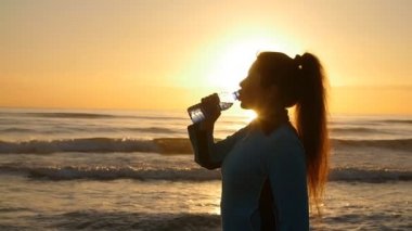 Genç sportif kadın içme suyu açık deniz kenarında Sunset'teki