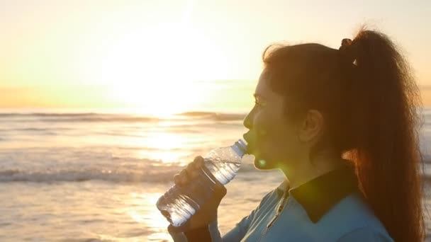 Νεαρή γυναίκα σπορ πόσιμο νερό εξωτερική ηλιοβασίλεμα κοντά στη θάλασσα — Αρχείο Βίντεο