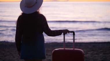 Sahilde bavulla şapkalı bir genç kadın