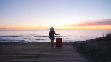 Sahilde bavulla şapkalı bir genç kadın