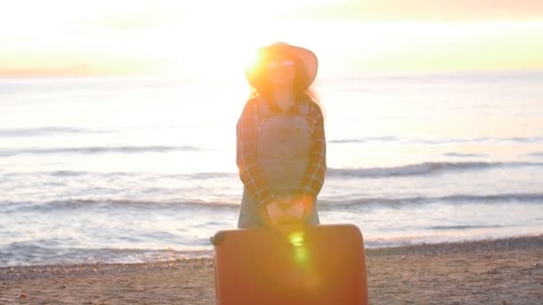 Giovane viaggiatrice con una valigia sulla spiaggia al tramonto — Video Stock