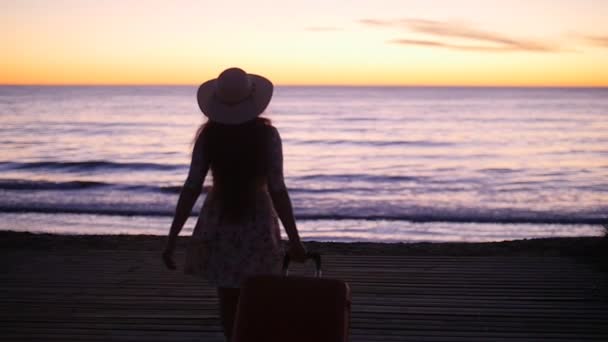 Junge Frau mit Hut bei Sonnenuntergang am Meer. Urlaubskonzept — Stockvideo