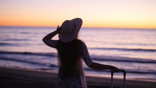 Jonge vrouw in de hoed bij zonsondergang in de buurt van de zee. Concept van vakantie — Stockvideo