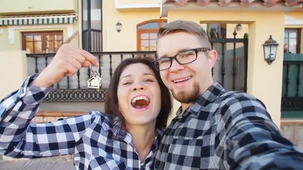 Jeune couple avec des clés debout à l'extérieur de la nouvelle maison et de prendre un selfie — Video