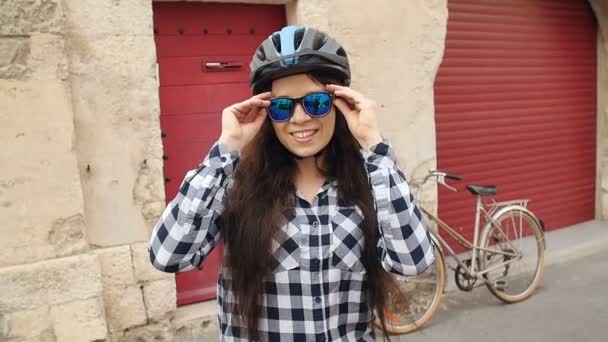 Молодая женщина-велосипедистка в очках и в шлеме улыбается и смотрит в камеру — стоковое видео