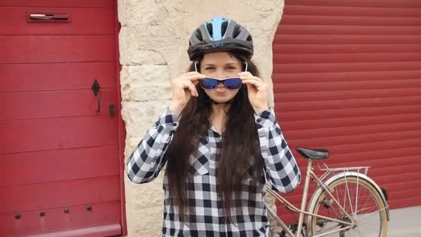 Молодая женщина-велосипедистка в очках и в шлеме улыбается и смотрит в камеру — стоковое видео