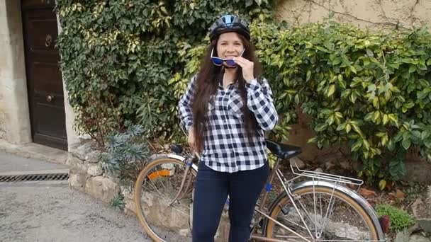 Gözlük takan ve gülümseyen ve kameraya bakarak bir kask giymiş genç kadın bisikletçi — Stok video