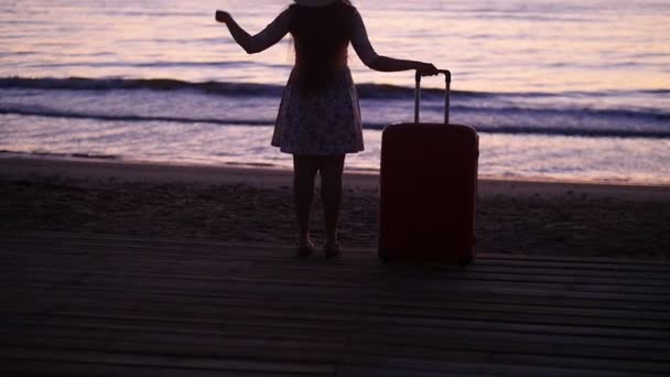 Junge schöne Frau mit Hut und großem Koffer am Strand — Stockvideo