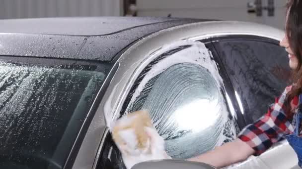 Молодая женщина моет машину губкой — стоковое видео