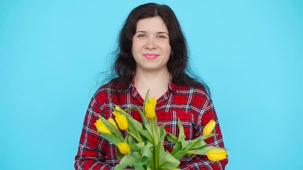 Молодая женщина с цветами тюльпанов в руках на синем фоне — стоковое видео