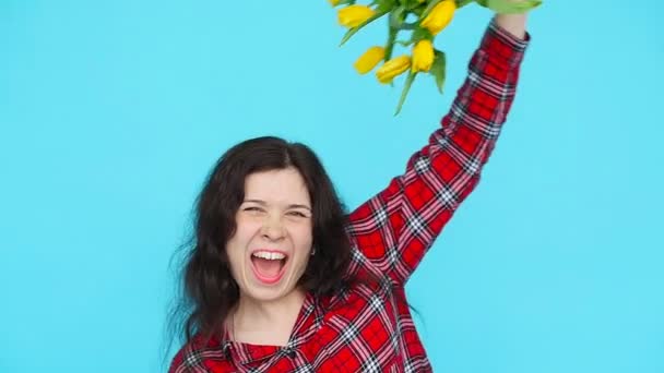 Молодая женщина с цветами тюльпанов в руках на синем фоне — стоковое видео