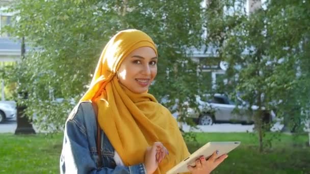 Boldog fiatal muszlim nő nyáron hidzsáb kezében digitális tabletta szabadban — Stock videók