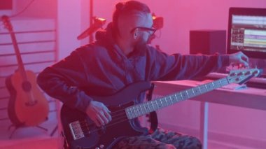 Hobi anlayışı ve müzik yapma. Genç sakallı adam bir müzik stüdyosunda bas gitar çalıyor.