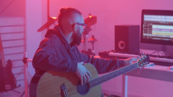 Concepto de hobby y hacer música. Joven barbudo toca la guitarra en un estudio de música casera — Vídeos de Stock