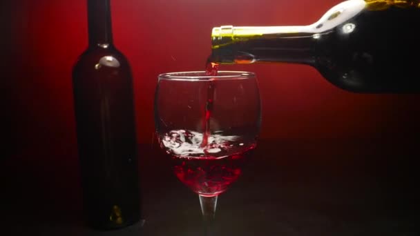 Red wine pouring into a wine glass on red background in slow motion — Stock Video