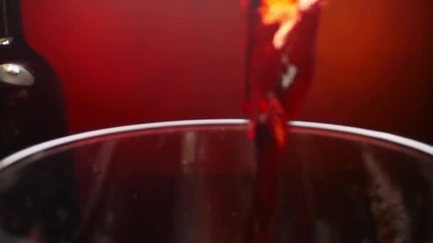 Κόκκινο κρασί ρίχνει σε ένα ποτήρι κρασί σε κόκκινο φόντο σε αργή κίνηση — Αρχείο Βίντεο