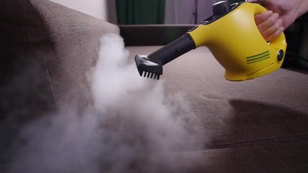 Koncepcja czyszczenia mebli i mieszkań. Mężczyzna sprzątanie kanapy z odkurzaczem parowym w domu — Wideo stockowe