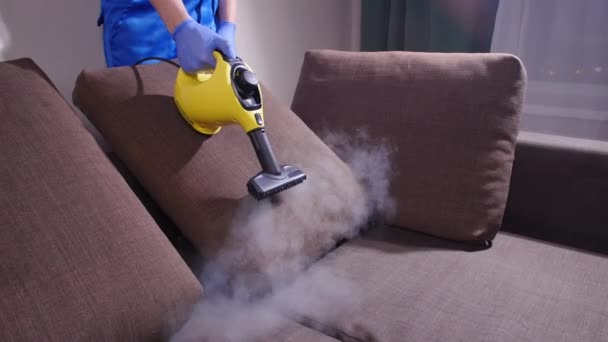 Концепция уборки фасадов и квартир. Мужчина чистит диван с пароочистителем дома — стоковое видео